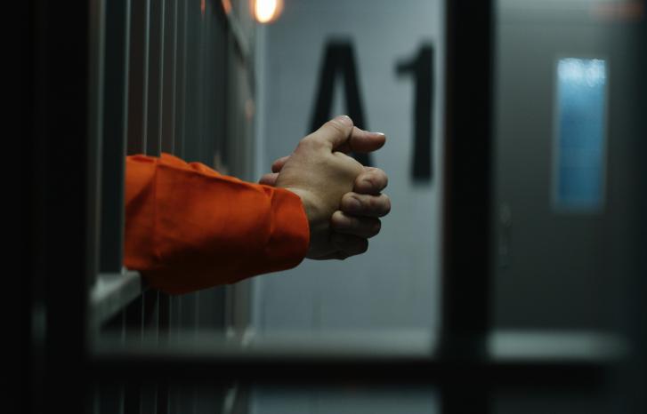 Mann i fengsel stikker hendene ut gjennom gitteret