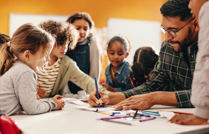 Mann. med skjegg og briller. tegner vet bord sammen med en gruppe barn