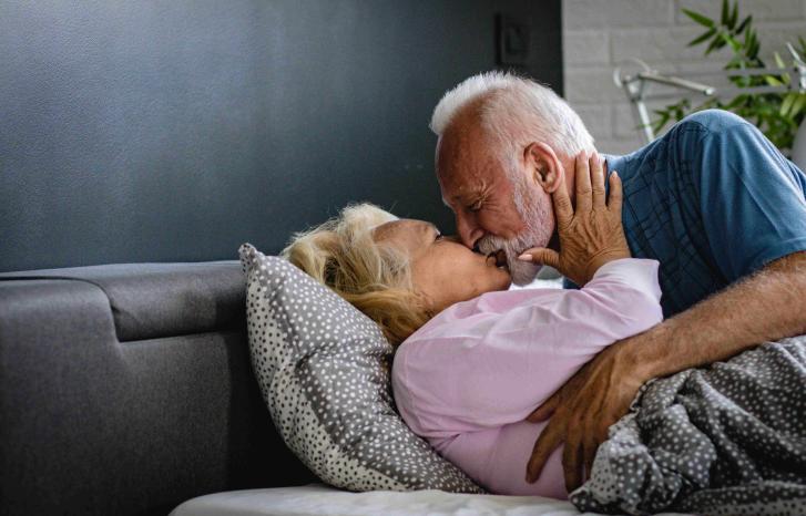 Eldre mann med skjegg omfavner eldre kvinne i sengen