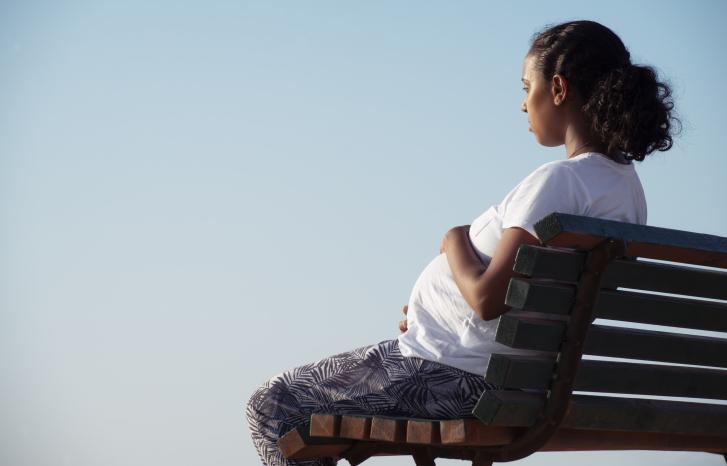 Gravid kvinne sitter på benk med ryggen til