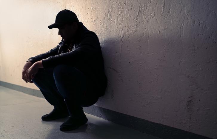 Mann sitter på huk inntil en vegg