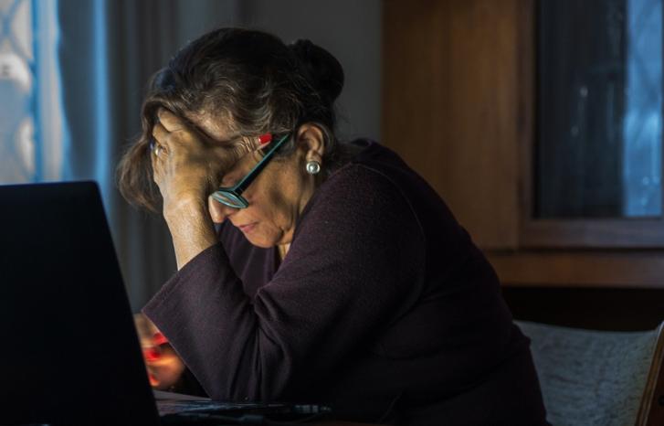 Eldre kvinne med bøyd hode foran pc'n