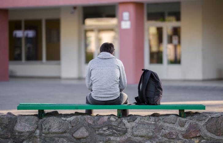 Gutt sittende med ryggen til på en benk i skolegården