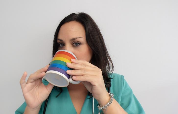 Ung kvinnelig helsearbeider drikker av kopp med regnbueflagg