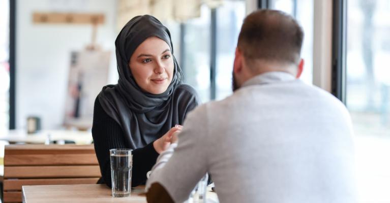 Kvinne med hijab og mann med ryggen til sitter på kafe
