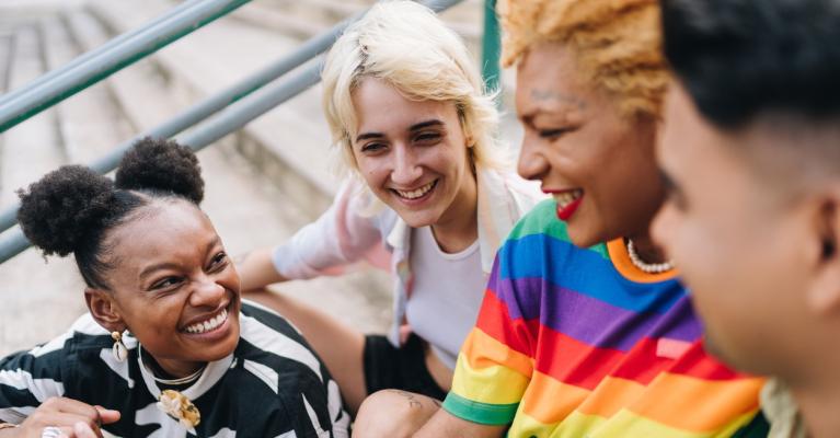 Skeive ungdommer med fargerike klær som prater og smiler, sittende i en trapp