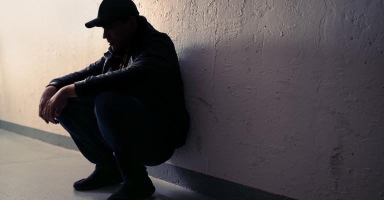 Mann sitter på huk inntil en vegg