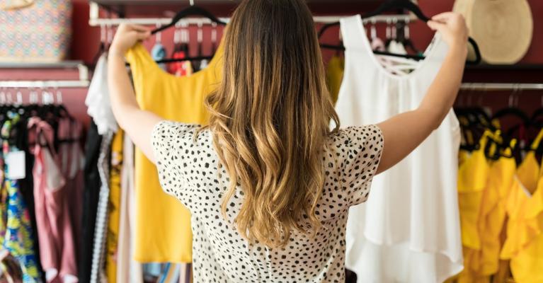 En ung kvinne i klesbutikk holder opp en gul og en hvit topp