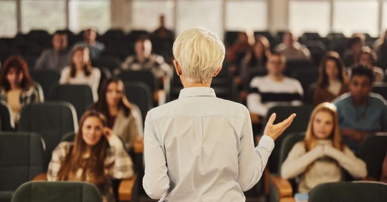 Kvinnelig foreleser med ryggen til foran et fullsatt auditorium