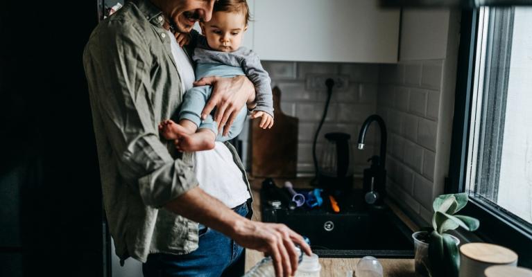 Far med lite barn på armen heller melk i flaske