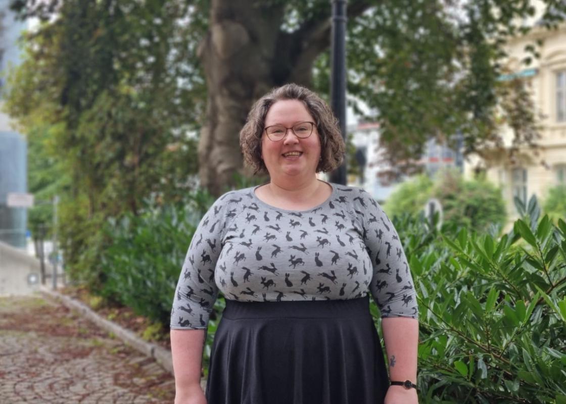Sunniva Árja Tobiasen, stipendiat ved senter for kvinne- og kjønnsforskning ved Universitetet i Bergen fotografert omgitt av grønne trær