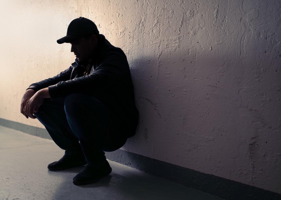 Mann sitter på huk inntil en vegg