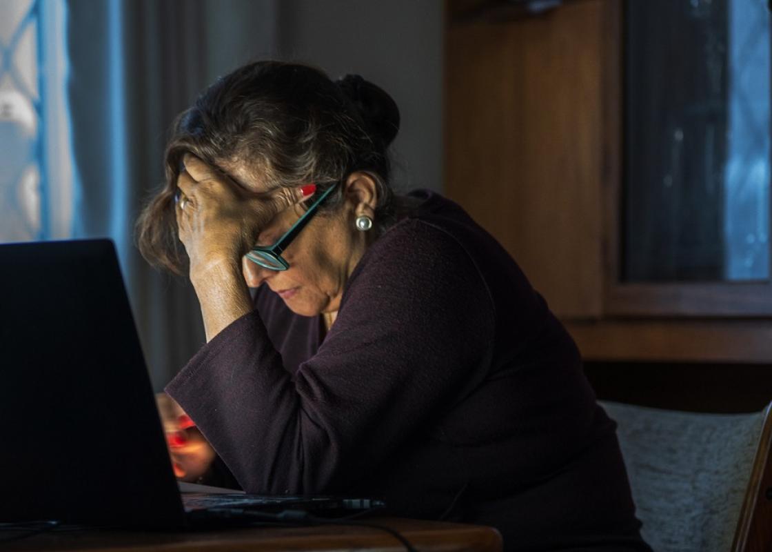 Eldre kvinne med bøyd hode foran pc'n
