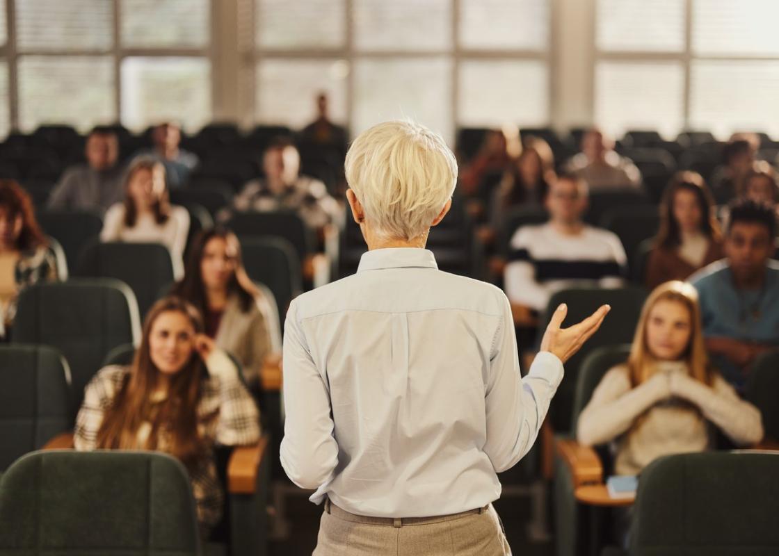 Kvinnelig foreleser med ryggen til foran et fullsatt auditorium