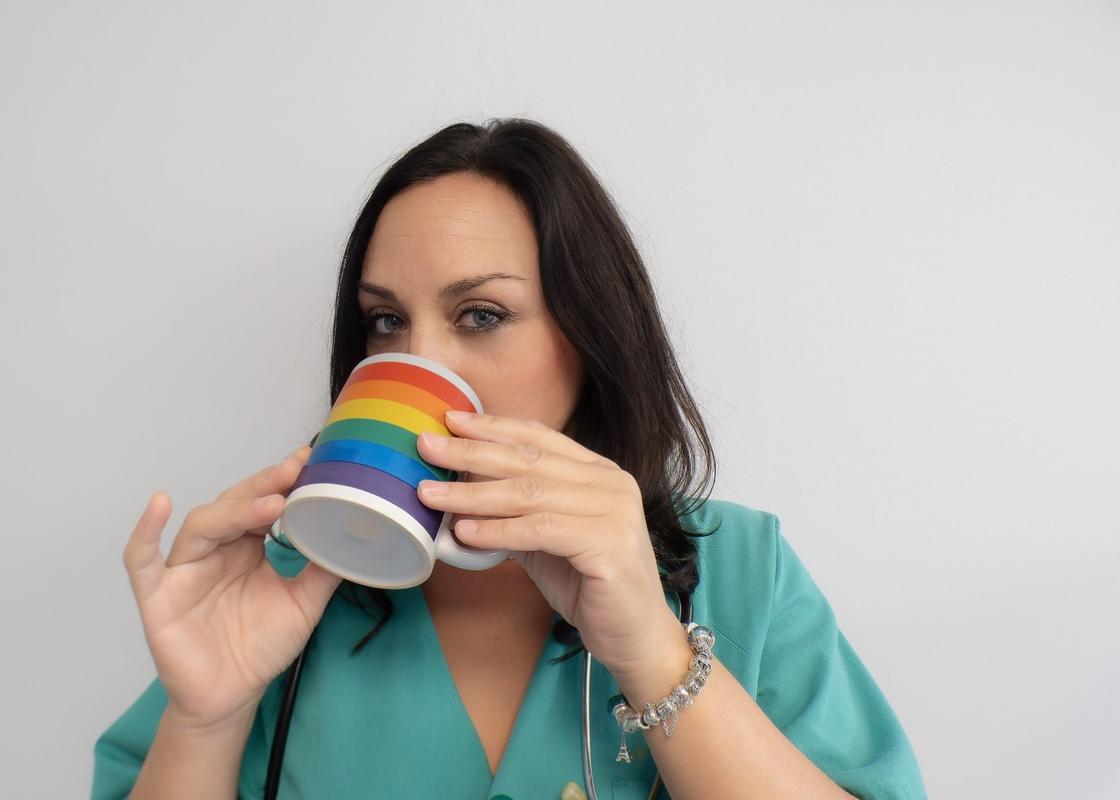 Ung kvinnelig helsearbeider drikker av kopp med regnbueflagg