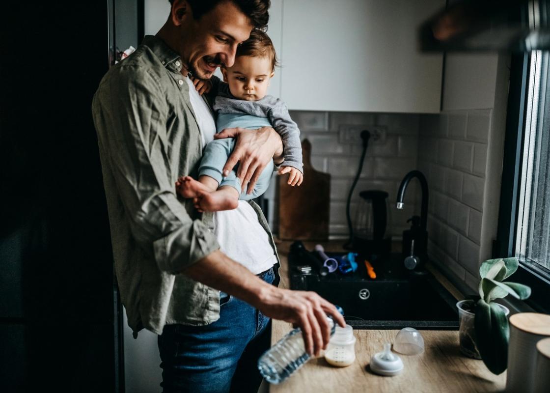 Far med lite barn på armen heller melk i flaske