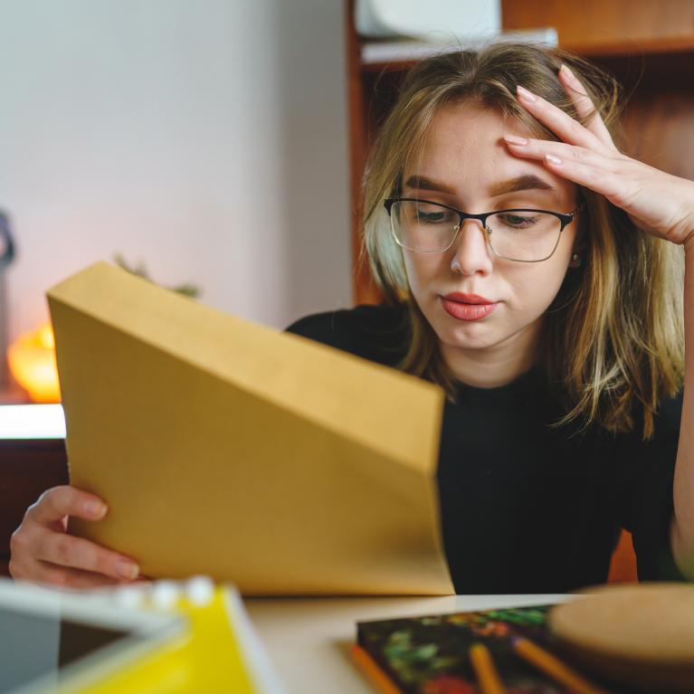 Jente eller ung kvinne med blondt og hår og briller som ser stresset ut og holder papir i den ene hånda Jente eller ung kvinne med blondt og hår og briller som ser stresset ut og holder papir i den ene hånda