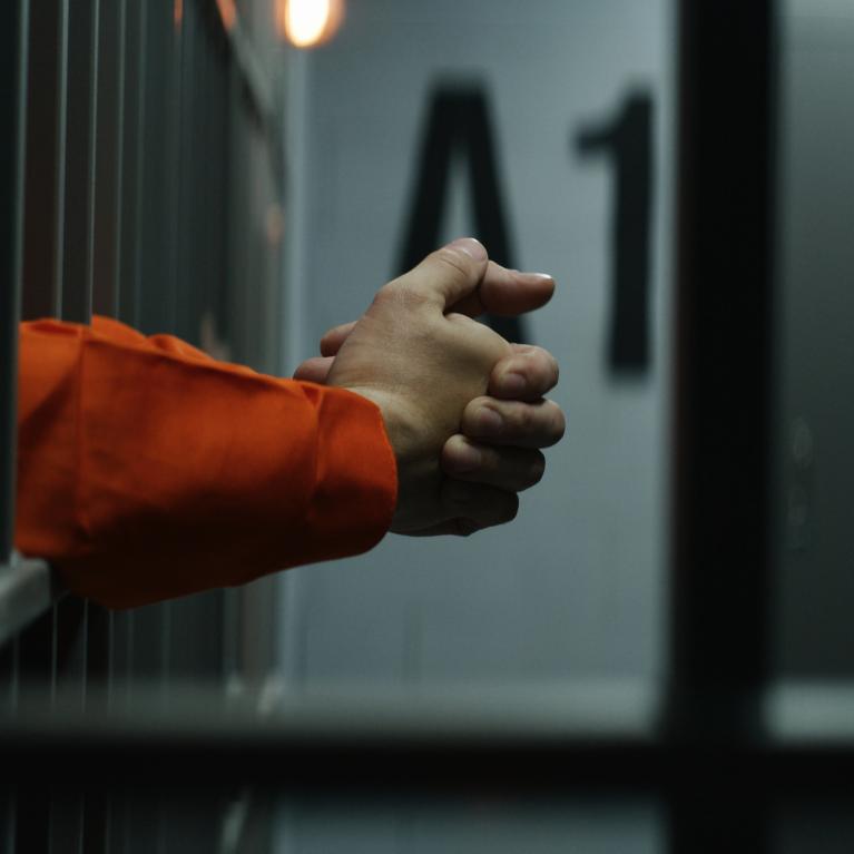 Mann i fengsel stikker hendene ut gjennom gitteret