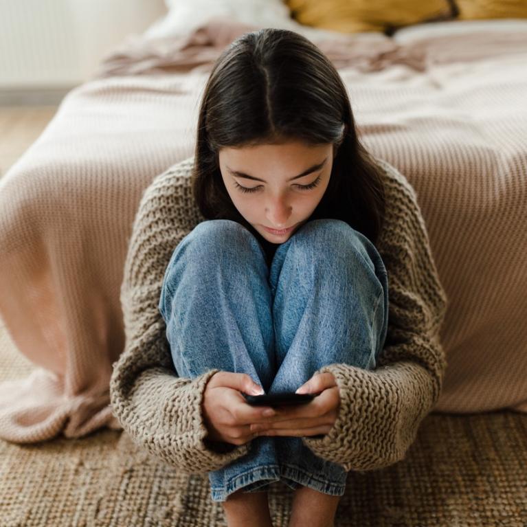 Ung jente sitter på gulvet og leser på mobilen sin