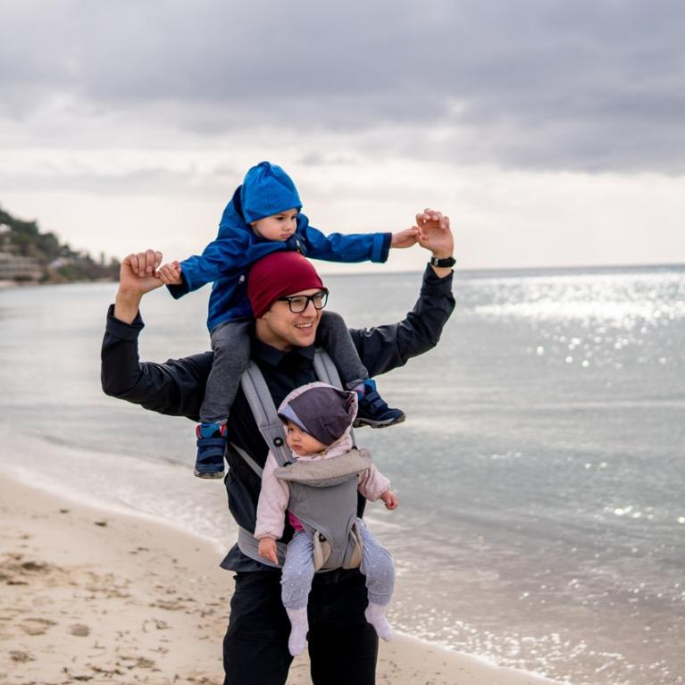 Pappa med to barn på stranden Pappa på tur på stranden med ett barn i bæresele og ett på nakken