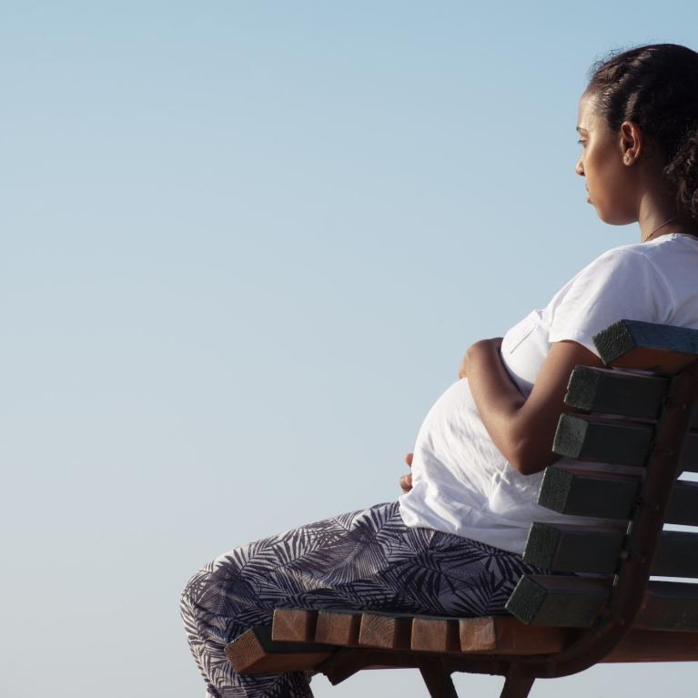 Gravid kvinne sitter på benk med ryggen til