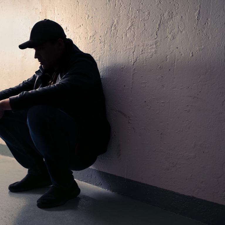 Mann sittende på huk Mann sitter på huk inntil en vegg