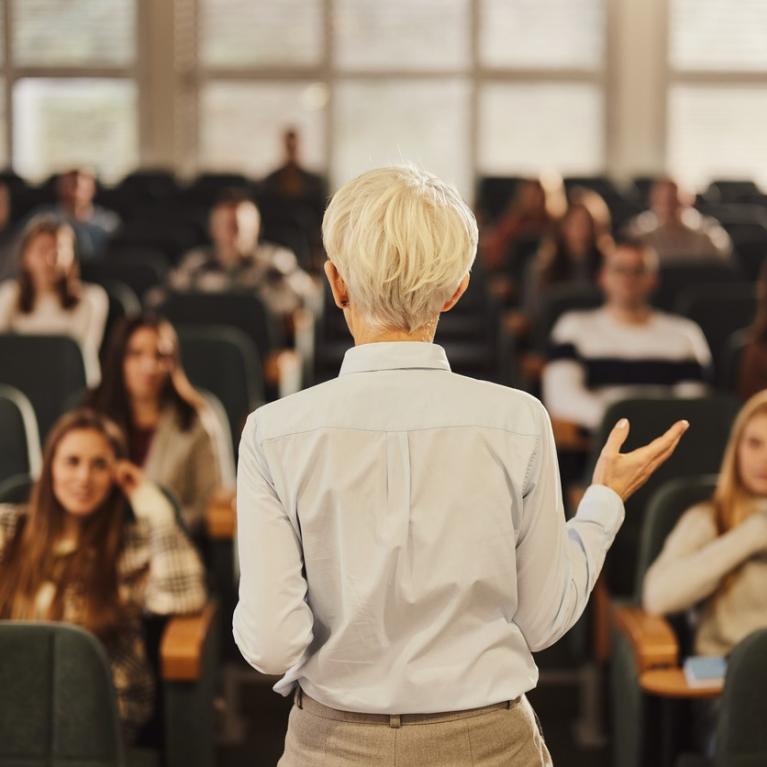 Kvinnelig foreleser med ryggen til foran et fullsatt auditorium
