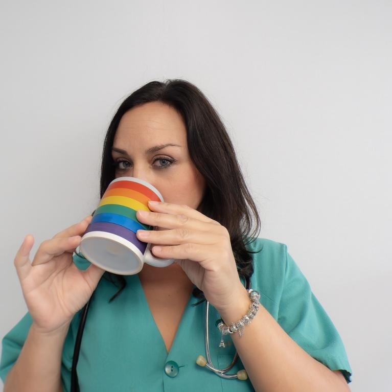 Ung kvinnelig helsearbeider drikker av kopp med regnbueflagg