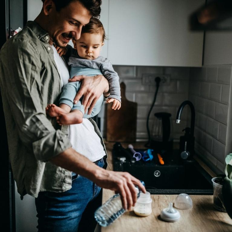 Far med lite barn på armen heller melk i flaske